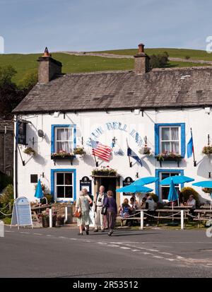 Gäste können sich unter Sonnenschirmen im malerischen Dorf Blue Bell Inn, Kettlewell, North Yorkshire, England, unterhalten und Getränke im Freien genießen. Stockfoto