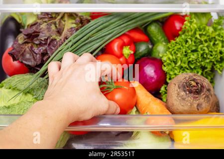 Mans Hand öffnet die Schublade des Kühlschranks mit Gemüse. Stockfoto