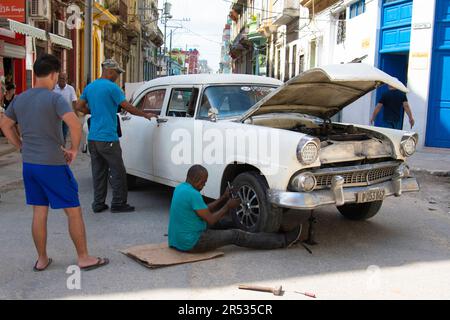 Ein Kubaner repariert den Reifen seines Autos in Havanna, Kuba, während andere Leute anhalten, zusehen und reden. Das Leben auf Kuba. Stockfoto