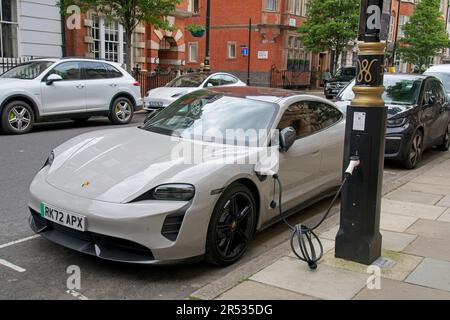 Harley Street London England UK Elektromotorwagen, der an der Straße aufgeladen wird, verbunden mit einem angepassten Leuchtenpfosten. Geparkte Fahrzeuge. Stockfoto