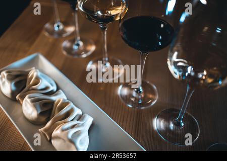 Georgianische Khinkali-Knödel mit Rot- und Weißwein in Gläsern auf einem Holztisch Stockfoto