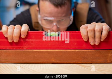 Qualitätskontrolle. Zimmermann mit Wasserwaage prüft die Höhe der Holzbohle Stockfoto
