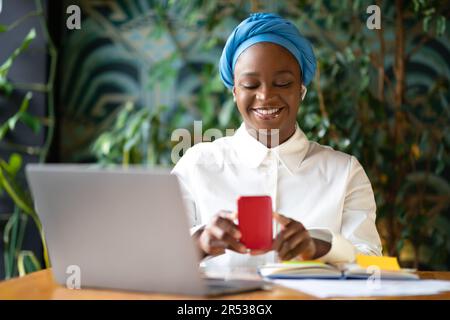 Glückliche junge schwarze Frau, die mehrere Aufgaben erledigt, Café-Inneneinrichtung Stockfoto