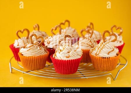 Eine Portion hausgemachter Karamell-Brezel-Cupcakes. Die Kuchen werden auf einem Kühlregal gezeigt und sind mit einer Brezel mit Buttercreme verziert Stockfoto
