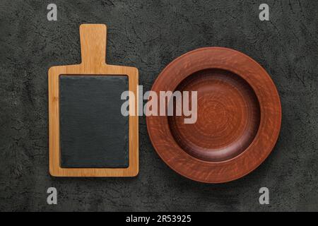 Braunes Holzschneidebrett mit Schieferstein, leere braune Tonplatte auf schwarzem Steintisch. Draufsicht mit Kopierbereich. Rustikale Gerichte Stockfoto
