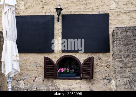 Das alte Steingebäude mit kleinen Fenstern und braunen Fensterläden Stockfoto