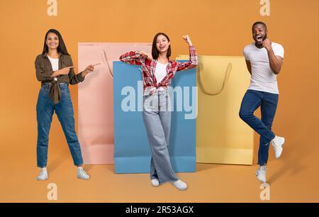 Fröhliche, multiethnische Jugendliche, die sich vor großen Einkaufstaschen posieren Stockfoto