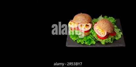 Köstliche Sandwiches mit Schinken, Tomaten, Käsescheiben und frischem Salat auf schwarzem Hintergrund mit Kopierbereich. Banner Stockfoto