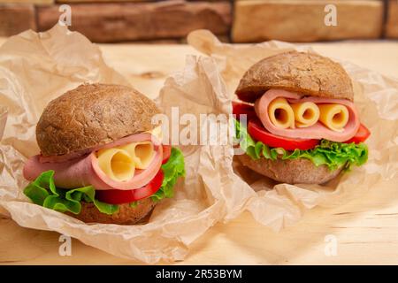 Leckere Sandwiches mit Schinken, Käse und frischem Salat, serviert auf Backpapier auf Holztisch Stockfoto