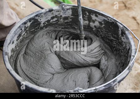 Kleber auf Zementbasis. Beton mit Elektrobohrer und Mischer mischen. Nassmörtel für Endbearbeitungsarbeiten im Bauwesen. Stockfoto