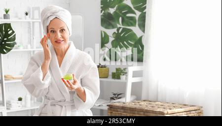 Schöne reife Frau, die Gesichtscreme im Badezimmer aufträgt Stockfoto