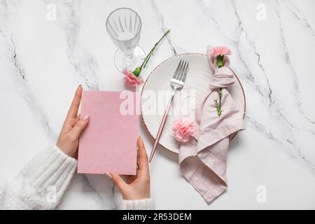 Frau mit leerer Einladungskarte neben Serviertisch mit Nelkenblumen Stockfoto