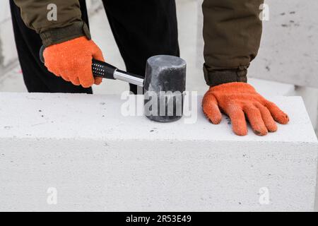 Bauarbeiter schlägt Porenbetonsteine mit einem Gummihammer. Stockfoto
