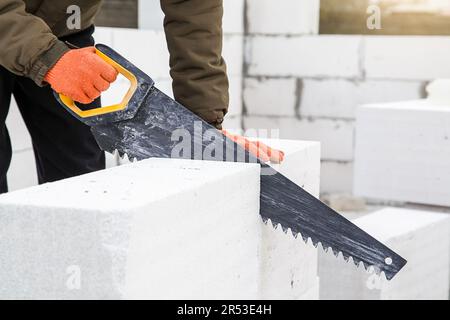 Sägen von Porenbetonblöcken mit Handsäge auf der Baustelle. Bauarbeiten, Bauarbeiten Stockfoto