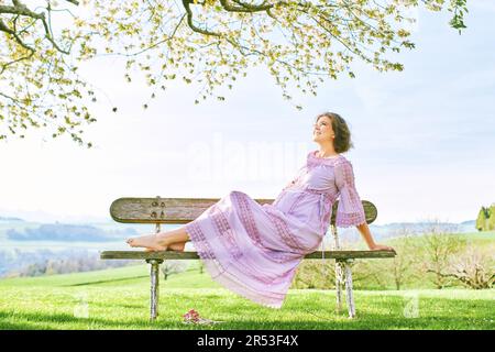 Außenporträt einer glücklichen schwangeren Frau, die einen schönen sonnigen Tag im Frühlingsgarten genießt Stockfoto