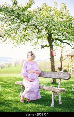 Außenporträt einer glücklichen schwangeren Frau, die einen schönen sonnigen Tag im Frühlingsgarten genießt Stockfoto