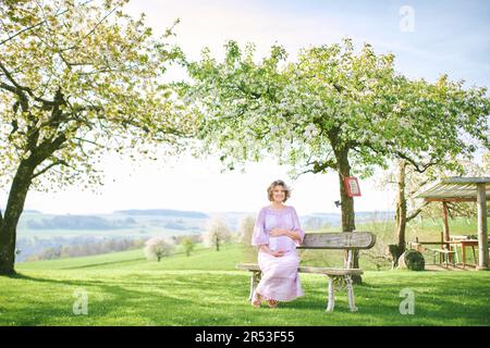 Außenporträt einer glücklichen schwangeren Frau, die einen schönen sonnigen Tag im Frühlingsgarten genießt Stockfoto