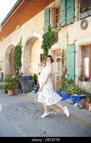 Außenporträt einer glücklichen, jungen schwangeren Frau, die auf der Straße auf dem Land tanzt Stockfoto