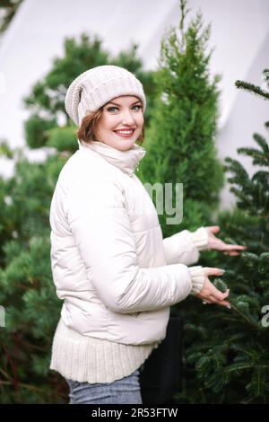Außenporträt einer glücklichen jungen Frau, die den weihnachtsbaum auf dem Markt auswählt Stockfoto