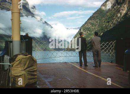 Geirangerfjord, Norwegen. Ca. 1960 Uhr – zwei Passagiere bewundern die Aussicht, während sie auf dem Deck einer Autofähre auf dem Geirangerfjord stehen. Stockfoto