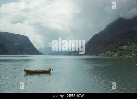 Skjolden, Norwegen. Ca. 1960 Uhr – Blick auf Lustrafjorden vom Dorf Skjolden in Vestland County. Ein kleines hölzernes Motorboot ist im Vordergrund sichtbar. Stockfoto