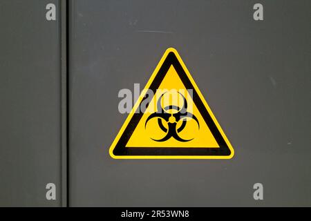 Gelbes Warnschild auf einer Metalltür vor „Biogefahr“. Stockfoto