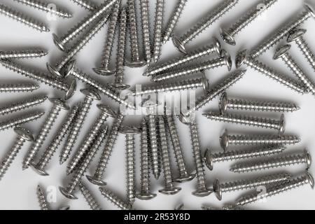 Auf dem Foto sehen Sie viele selbstschneidende Schrauben aus weißem Stahl, die in einem Schlamassel herumliegen. Sie können zum Befestigen verschiedener Materialien im Innen- und Außenbereich verwendet werden. Stockfoto