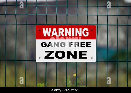 Rot ein weißes Warnschild an einem Zaun mit der Aufschrift „Warnung - Gang free Zone“ und einer Leerstelle darunter. Stockfoto