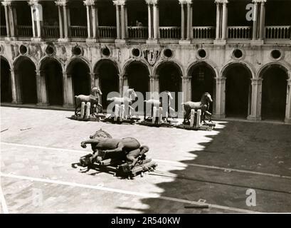 1945 , Venedig , ITALIEN : das PFERD der italienischen Bronzestatue von Condottiero BARTOLOMEO COLLEONI ( 1395 - 1475 ) von ANDREA DEL VERROCCHIO ( 1435 - 1888 ) an den letzten Tagen des Zweiten Weltkriegs . Verrochios Reiterstatue Colleoni wird aus dem Keller des Herzogspalastes entfernt , bevor sie auf den Platz vor der Heiligen Johannes und Paul zurückgebracht wird . Die vier Bronzepferde ( im Hintergrund ) von St. Marks sind die meistgereisten Pferde der Geschichte. Obwohl ihre Herkunft unbekannt ist, wird angenommen, dass sie ein griechisches Werk der hellenistischen Zeit sind. Nach der Eroberung Griechenlands Stockfoto