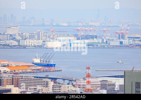 Das Frachtschiff legte im Hafen von Kobe an, Ladekräne und die Skyline der Stadt waren in der Ferne Stockfoto