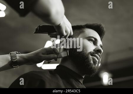 Professioneller Friseur, der mit dem Kunden im Friseursalon arbeitet, niedrige Sicht. Schwarzweiß-Effekt Stockfoto