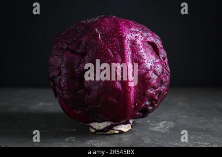 Ein frischer, reifer Rotkohl mit Wassertropfen auf einem grauen Tisch vor dunklem Hintergrund Stockfoto