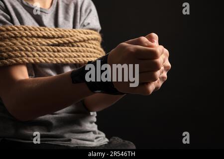 Ein kleiner Junge gefesselt und als Geisel genommen, auf dunklem Hintergrund, Nahaufnahme Stockfoto