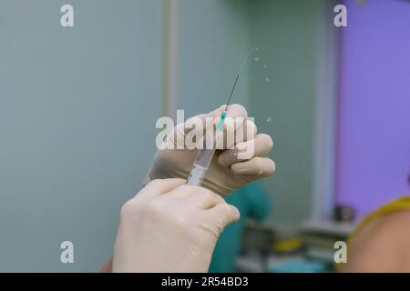 Der Arzt füllt die Spritze mit dem Medikament, während er die Verabreichung des Patienten während der Behandlung vorbereitet Stockfoto