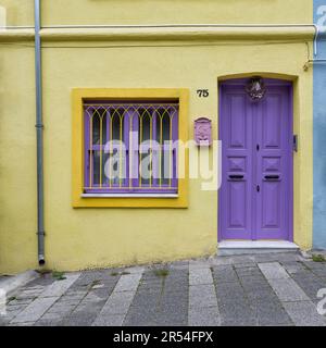 Außenfassade eines Wohngebäudes mit gelb und violett bemalten Wänden, violette Tür und schmiedeeiserne Fenster, in einer engen Straße, Uskudar Viertel, Istanbul, Türkei Stockfoto