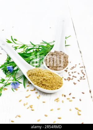 Leinenkleie und Mehl in zwei Löffeln, Samen auf dem Tisch, Leinenblätter und Blumen auf dem Hintergrund von Holzbrettern Stockfoto