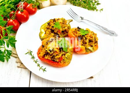 Pfeffer süß, gefüllt mit Pilzen, Tomaten, Couscous und Käse auf einem weißen Teller auf Handtuch, Gabel, Petersilie vor dem Hintergrund von Holzbrettern Stockfoto
