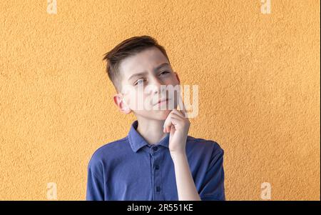 Ein emotionales Porträt eines Teenagers. Ein grüblerischer Teenager, isoliert auf gelbem Hintergrund. Ein ernstes, aufmerksames Kind. Stockfoto