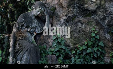 Skulptur einer schönen trauernden Frau auf einem Friedhof. Sie lehnt sich auf einen unangebrachten Stein. Stockfoto