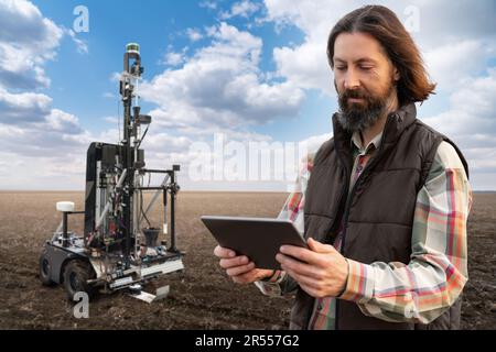 Der Landwirt steuert den autonomen Roboter zur Messung der Bodenqualität auf einem landwirtschaftlichen Feld. Konzept der intelligenten Landwirtschaft. Stockfoto