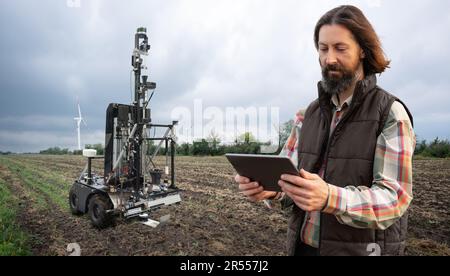 Der Landwirt steuert den autonomen Roboter zur Messung der Bodenqualität auf einem landwirtschaftlichen Feld. Konzept der intelligenten Landwirtschaft. Stockfoto