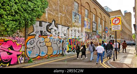 London Brick Lane Tower Hamlets Geschäfte Cafés Restaurants große Mauer in der Buxton Street mit Gaffiti und Tourgruppe Stockfoto