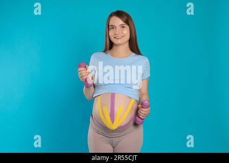 Schwangere Frau mit Kinesio-Bändern auf dem Bauch, die Übungen vor hellblauem Hintergrund macht Stockfoto