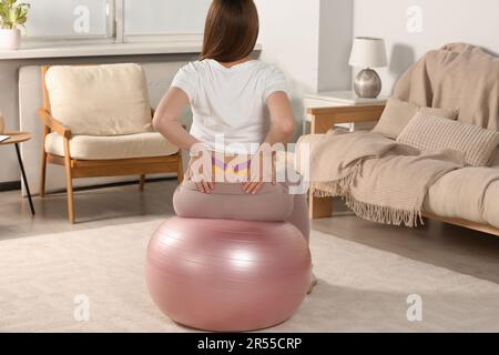 Schwangere Frau mit Kinesio-Videos, die zu Hause Sportball-Übungen macht, Rückansicht Stockfoto