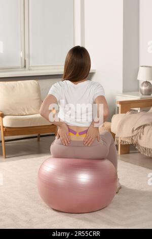 Schwangere Frau mit Kinesio-Videos, die zu Hause Sportball-Übungen macht, Rückansicht Stockfoto