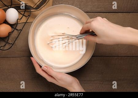 Frau, die Zutaten mit Schneebesen auf einem Holztisch schlägt, Draufsicht. Ich koche leckeren Eierlikör Stockfoto