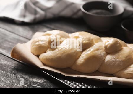 Rohes geflochtenes Brot und Zutaten auf schwarzem Holztisch, Nahaufnahme. Traditionelle Sabbat-Challah Stockfoto