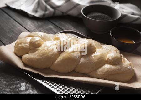 Rohes geflochtenes Brot und Zutaten auf schwarzem Holztisch, Nahaufnahme. Traditionelle Sabbat-Challah Stockfoto