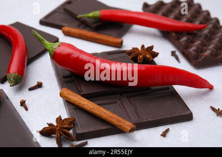 Köstliche Schokolade, frische rote Chili-Paprika und Gewürze auf weißem Tisch, Nahaufnahme Stockfoto