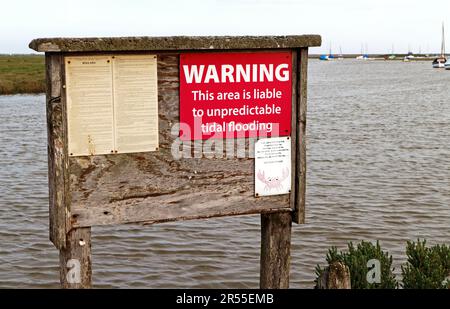 Ein Warnschild für unvorhersehbare Gezeitenüberschwemmungen am Kai im Hafen an der Nordnorfolkküste in Blakeney, Norfolk, England, Großbritannien. Stockfoto